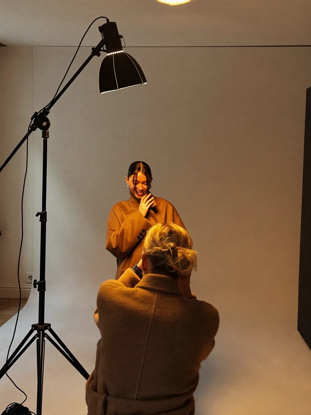 A photographer shooting a model in a camel coat in a fashion studio